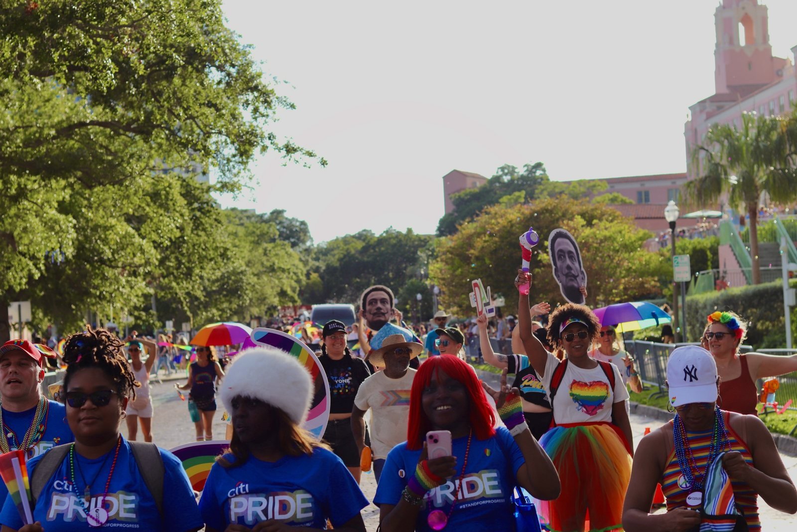 Pride marchers in blue team shirts walking toward the camera through a crowded parade route