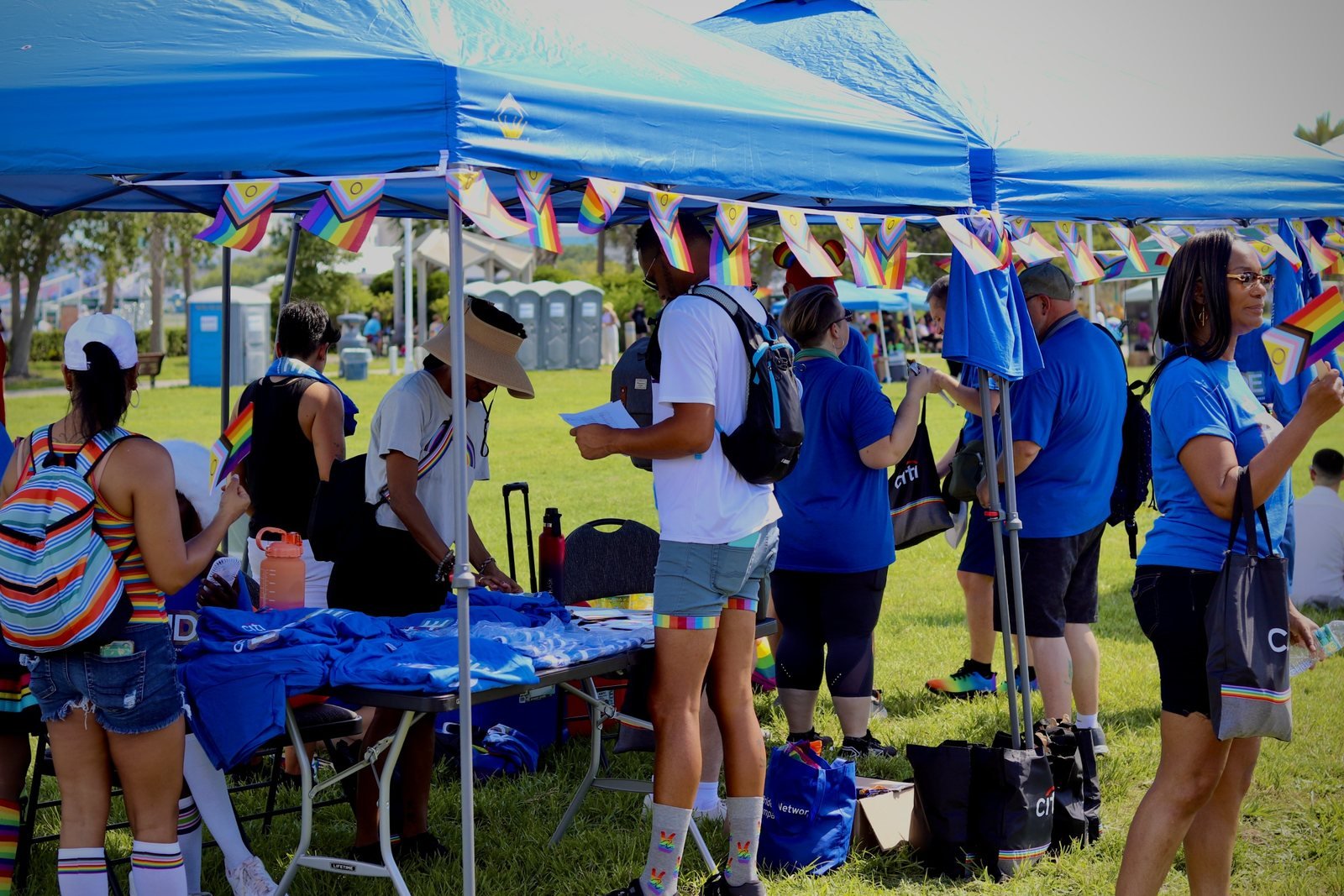 Volunteers sorting shirts under blue tents decorated with Pride flags