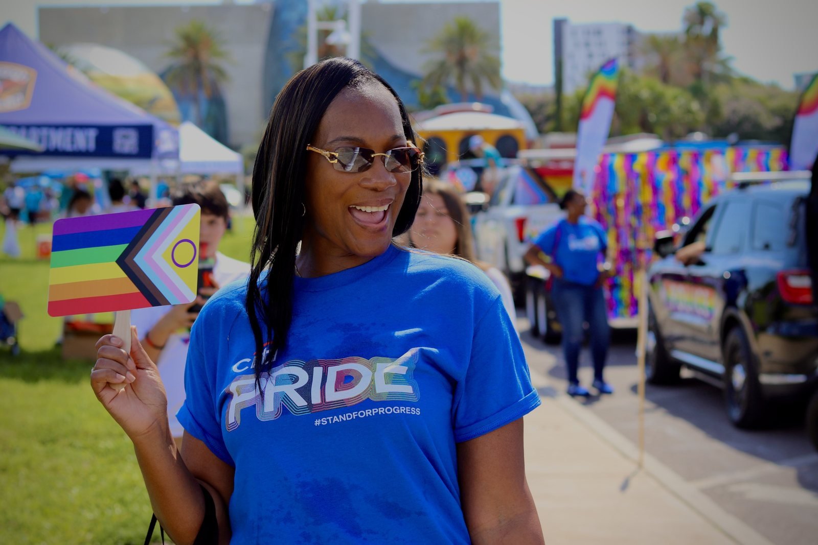 Woman in a blue Pride shirt laughing and holding a Progress Pride flag