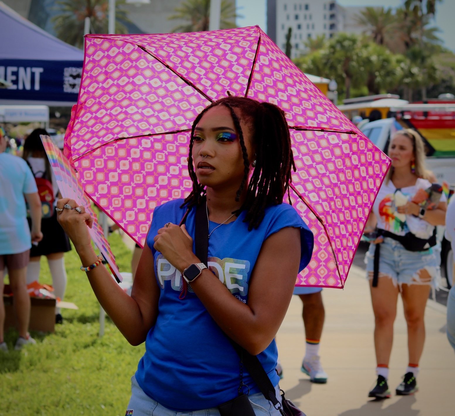 Woman under a pink patterned umbrella holding a rainbow fan
