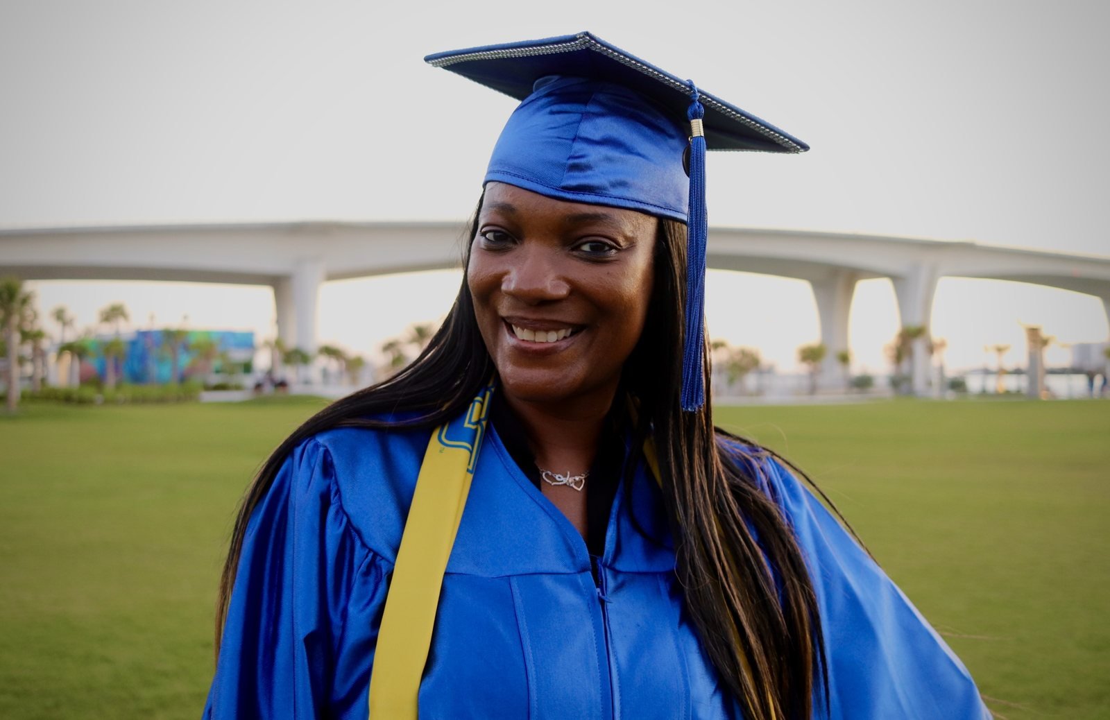 Graduate in a blue cap and gown smiling outdoors