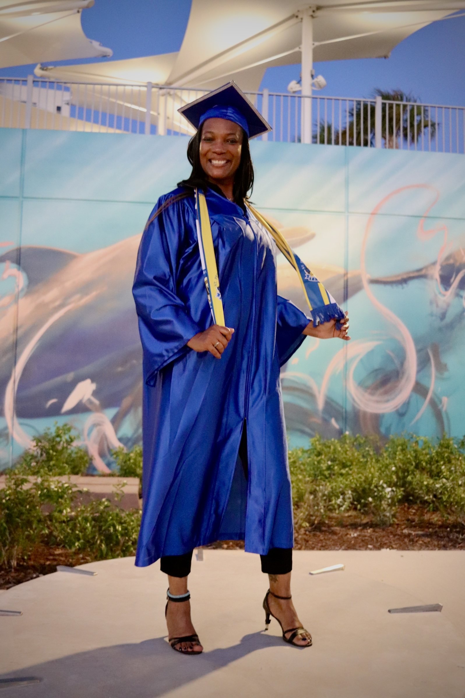 Graduate in a blue cap and gown standing outdoors