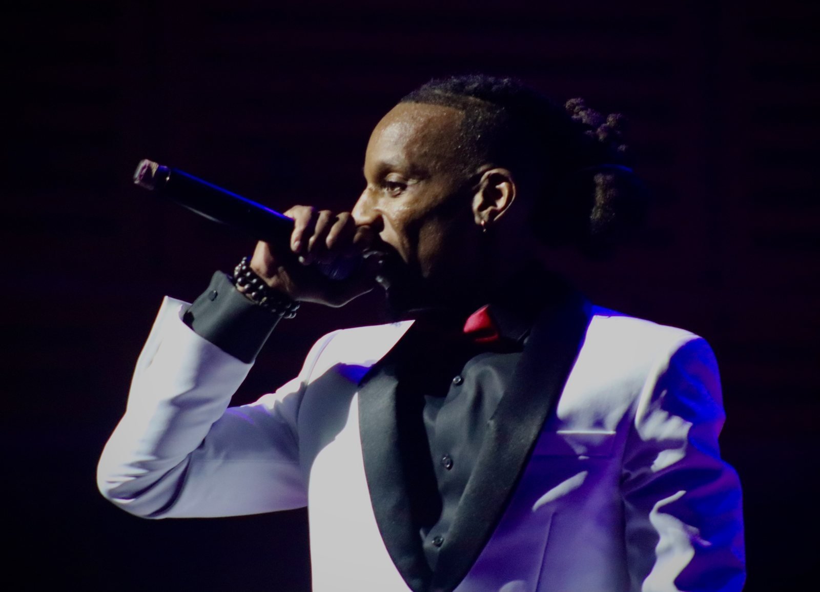 Man speaking on stage in a white tuxedo jacket