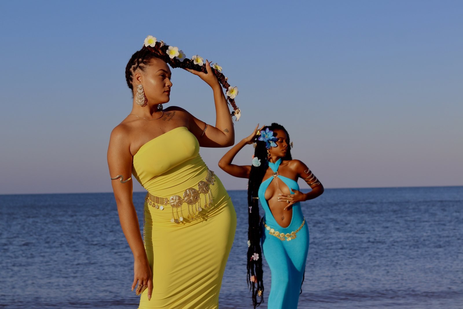Two women in bright dresses posed beside the ocean