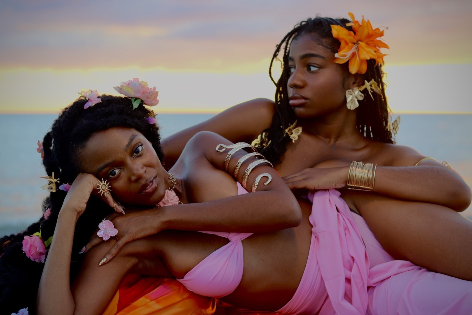 Two women posed together beside the water at sunset